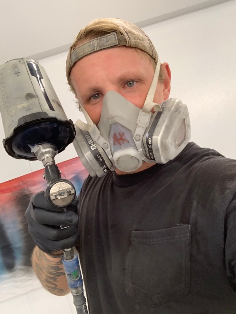 person holding spray gun facing and pointing camera selfie